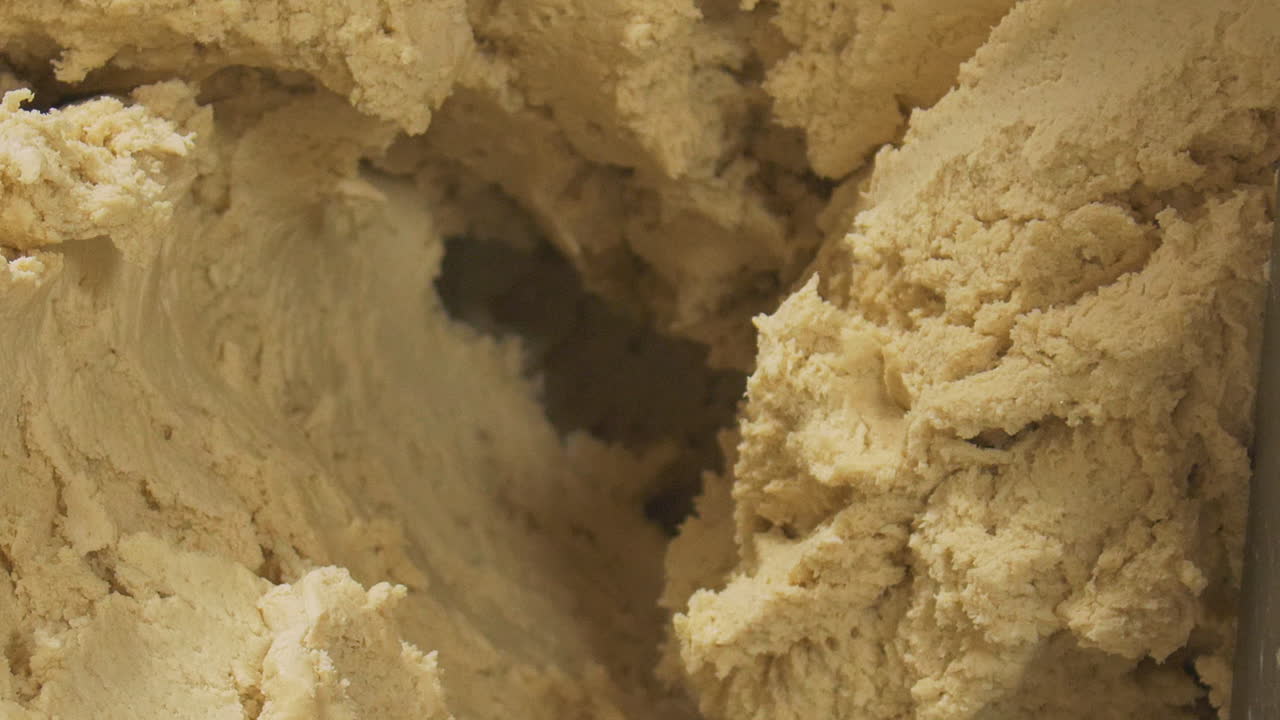Heavy chunks of dough are picked up by hand out of an industrial sized food mixer