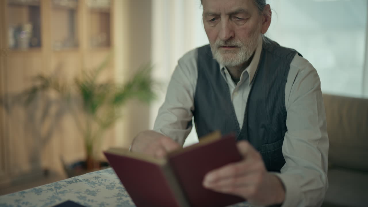 Anziano concentrato che legge un libro e gira le pagine a casa