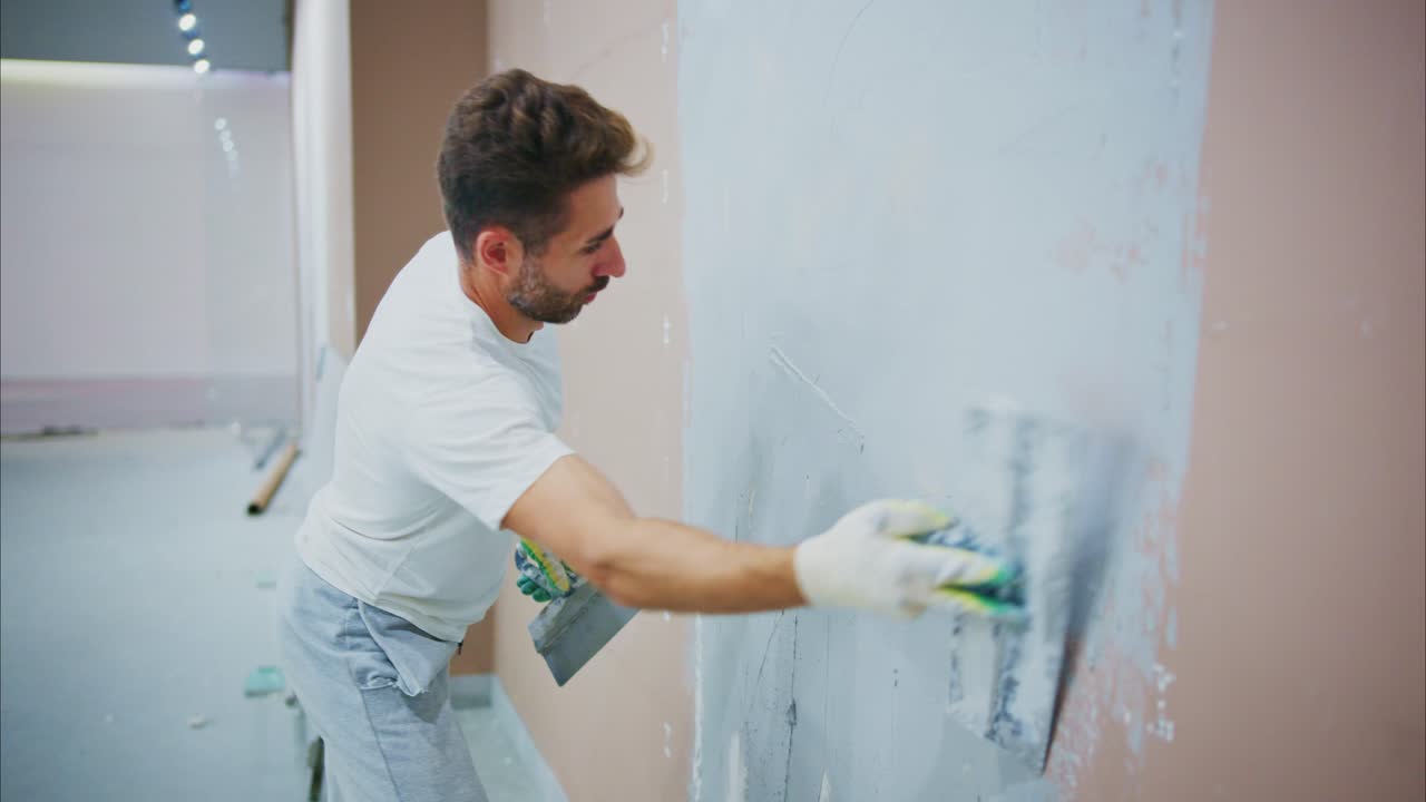A skilled worker meticulously applies a finishing coat of plaster to a wall, demonstrating craftsmanship and dedication in a newly renovated space, preparing for the final touch