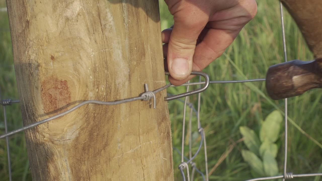 목초지 인클로저용 나무 기둥에 짠 철조망 울타리 스테이플을 망치질하는 것
