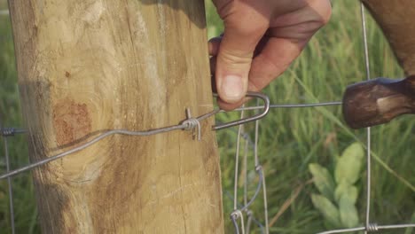 martillado de grapas de valla de alambre tejido en un poste de madera para recinto de pasto