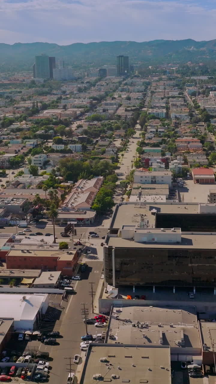 Few multi-storied buildings standing out among the low architectural scenery of LA, USA. Drone footage over the sunny metropolis at daytime. Vertical video
