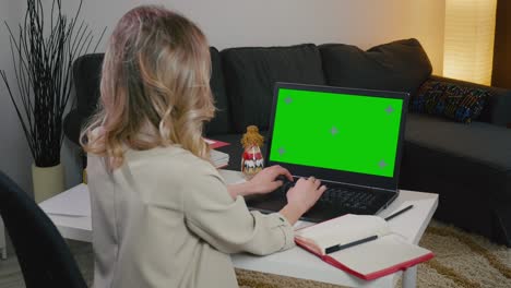 business woman at home typing on laptop with green screen chroma key display.