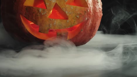 carved halloween pumpkin jack-o-lantern with candles in it on dark table with white smoke. slow motion. close up shooting. 4k