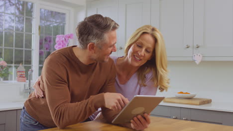 pareja madura en casa en la cocina usando una tableta digital para reservar espectáculos, vacaciones o hacer compras juntos - filmado en cámara lenta