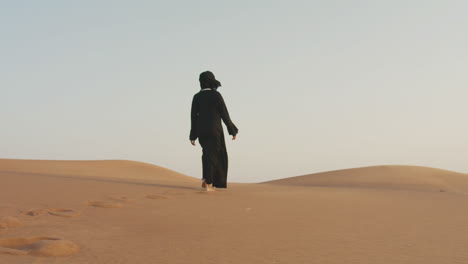 follow me shot of a beautiful muslim woman with hijab walking barefoot in a windy desert