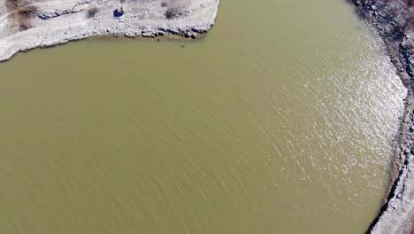 Top-down-view-of-the-lake-shoreline-with-predominantly-murky-water-and-harsh-limited-vegetation