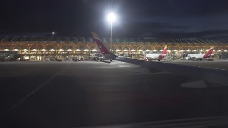 vista nocturna del aeropuerto de madrid desde una ventana de avión terminal t4 y ala de avión visible durante la hora azul de aterrizaje