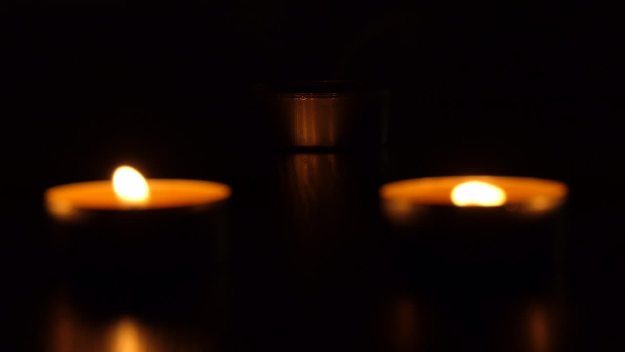 The candle flickers in the dark. A white round candle burns on a dark background. Round candles burn and go out. Sorrow. Romance. Joy. 4K video