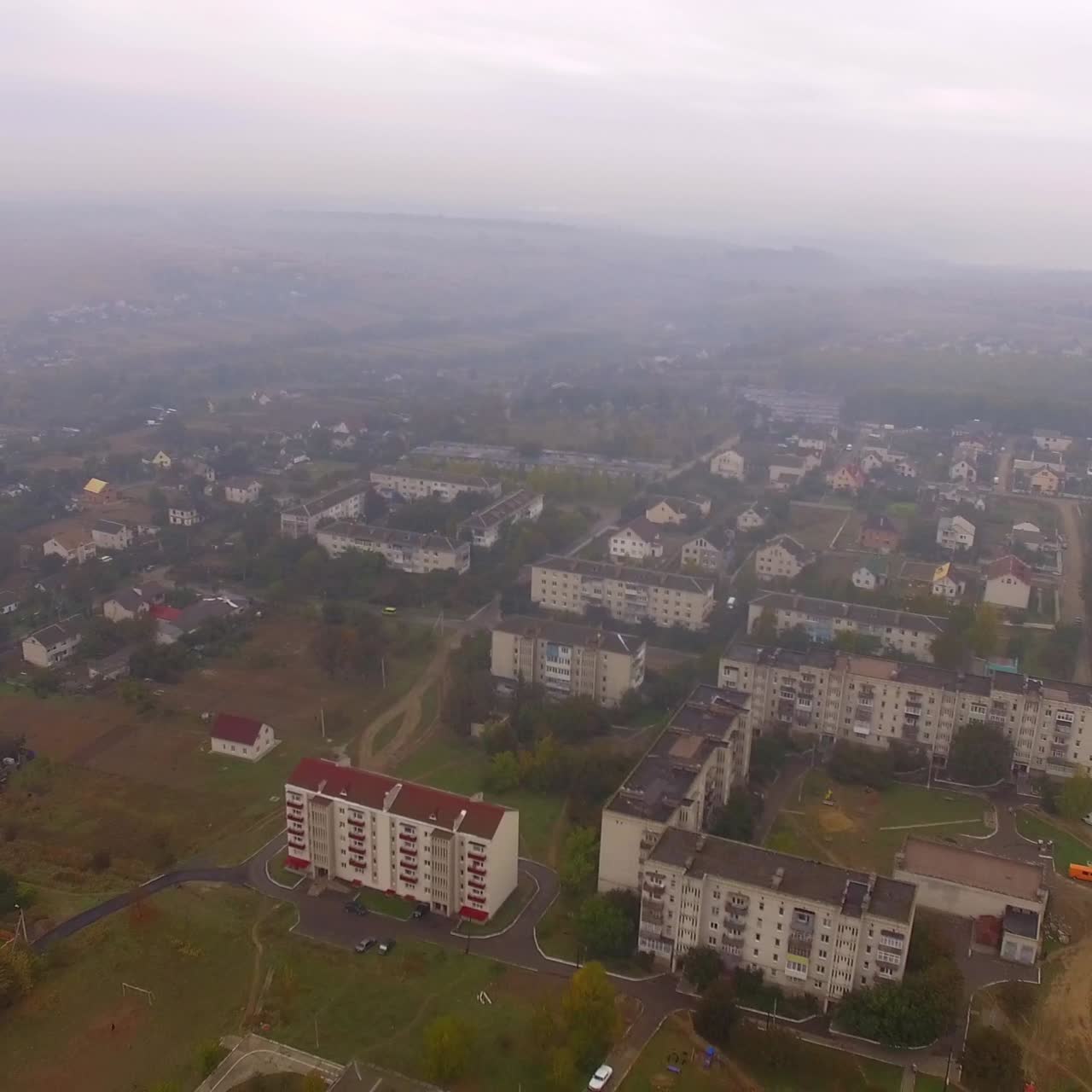 Fog covered usual big city with residential areas and stadium. Drone footage over the city on gloomy autumn day