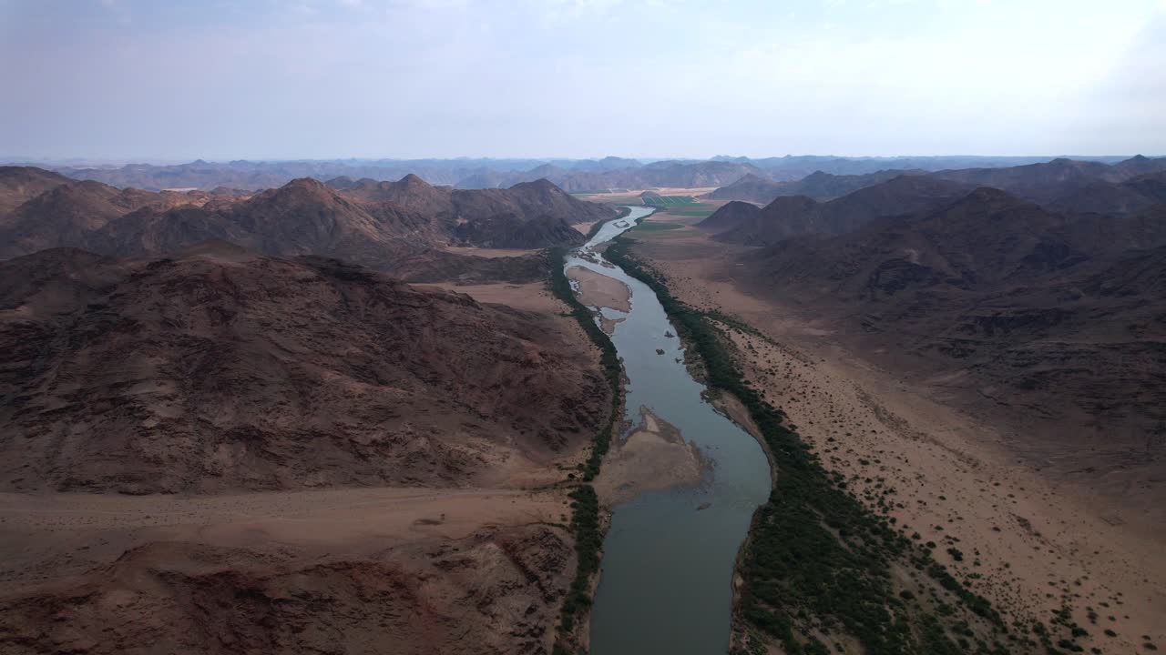 Elevated aerial over Orange River revealing lush green banks, arid desert terrain, and dramatic distant mountain peaks in the African wilderness