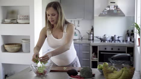 futura madre pacífica cortando ensalada en la mesa de la cocina