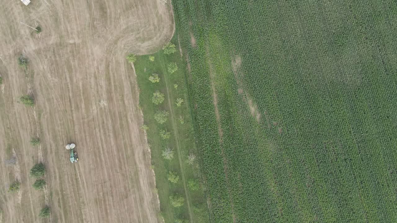 disparo aéreo de un tractor que se mueve en un campo para dejar caer una bala de heno, con un avión no tripulado que realiza un movimiento lateral para capturar la escena