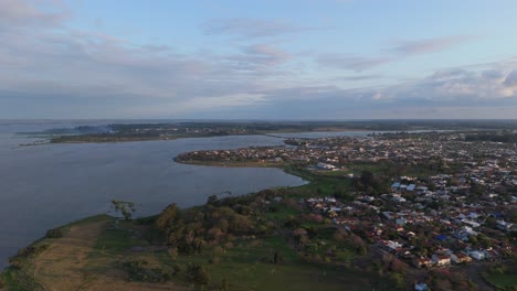 aerial shot of a town beside a large river at dusk showcasing houses, greenery, and a serene environment, harmonising urban and natural elements of federacion, entre ríos, argentina