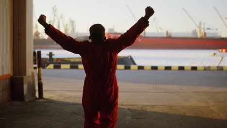 silhouette of a worker in orange uniform walking through the harbour storage by the sea during his break and raising his hands