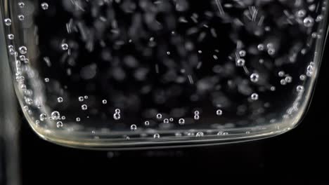 close up of mineral water bubbles in the glass. macro shop of carbonated fresh sparkling drink with oxygen balls on dark background