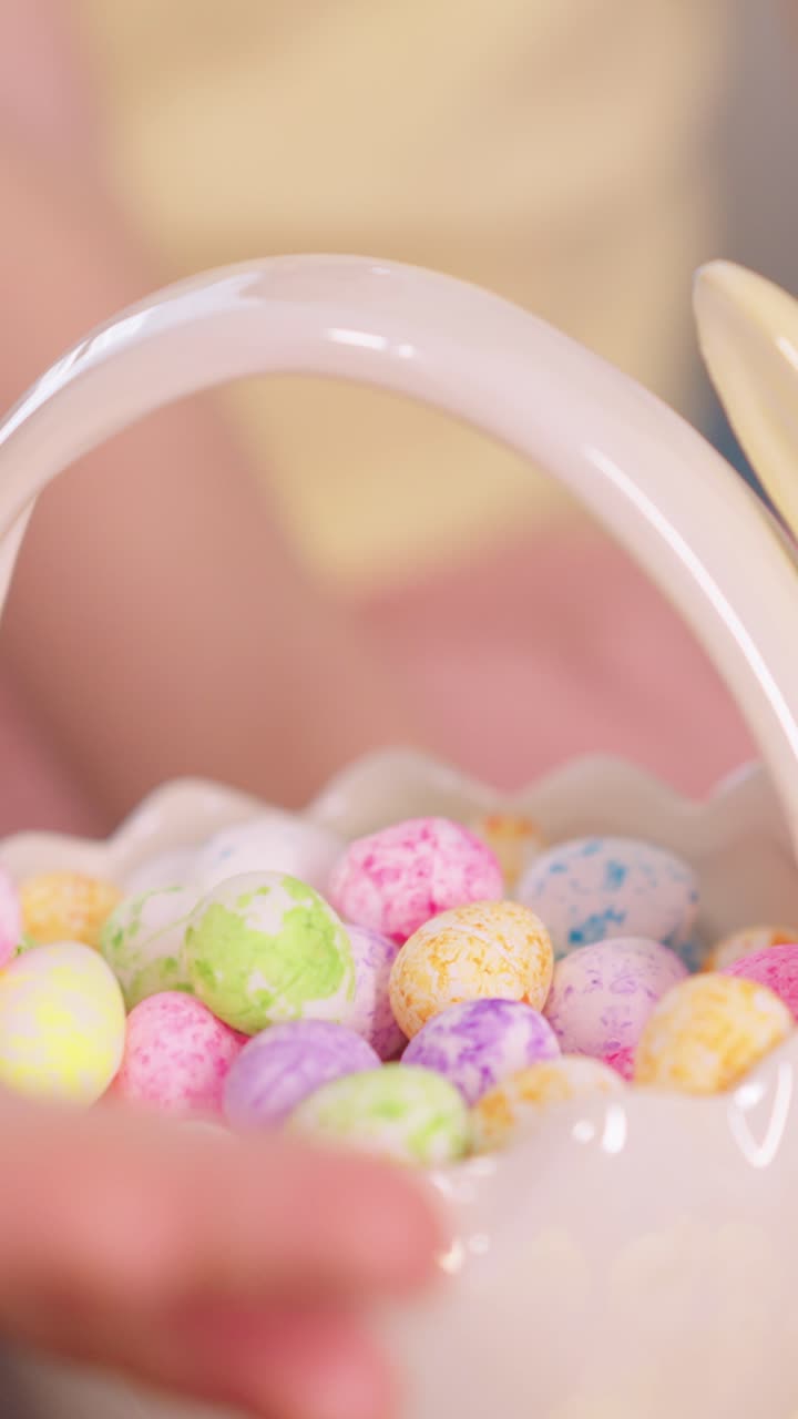 Mão de Criança Enchendo uma Cesta de Páscoa Branca com Ovos de Chocolate Coloridos