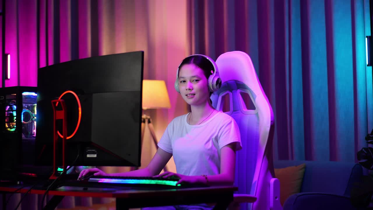 una adolescente asiática sonriendo a la cámara y mostrando el pulgar hacia arriba mientras juega videojuegos en la computadora