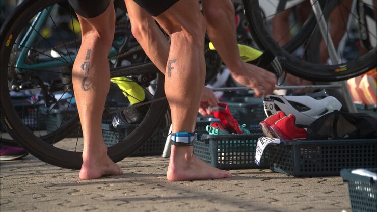 Primo piano al rallentatore di un atleta uomo che conclude la frazione di ciclismo a un triathlon, preparandosi per la frazione di corsa nella zona di transizione