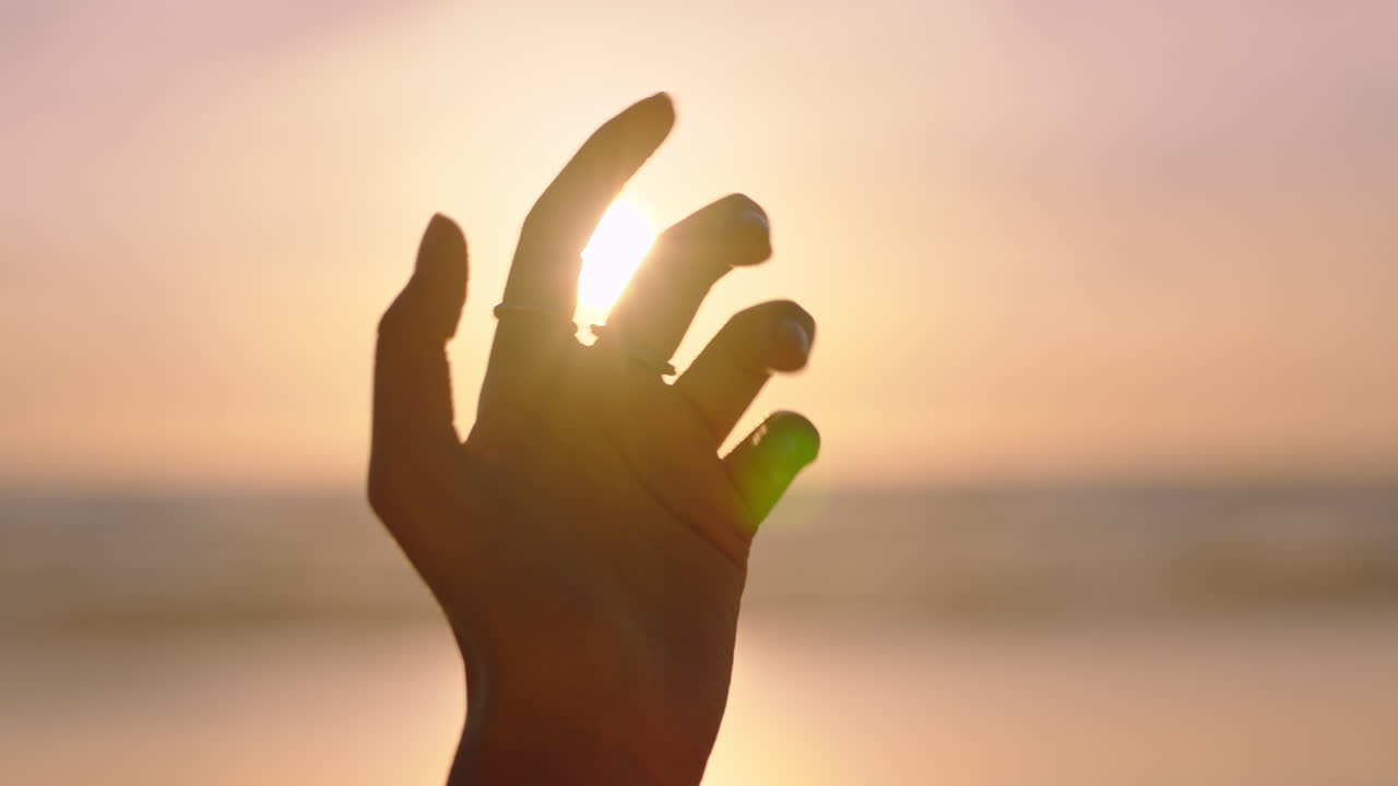 cerca de la mano de la mujer alcanzando la luz del sol en la playa jugando con los rayos dorados al atardecer