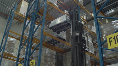 high forklift placing pallet filled with boxes on high shelf in warehouse