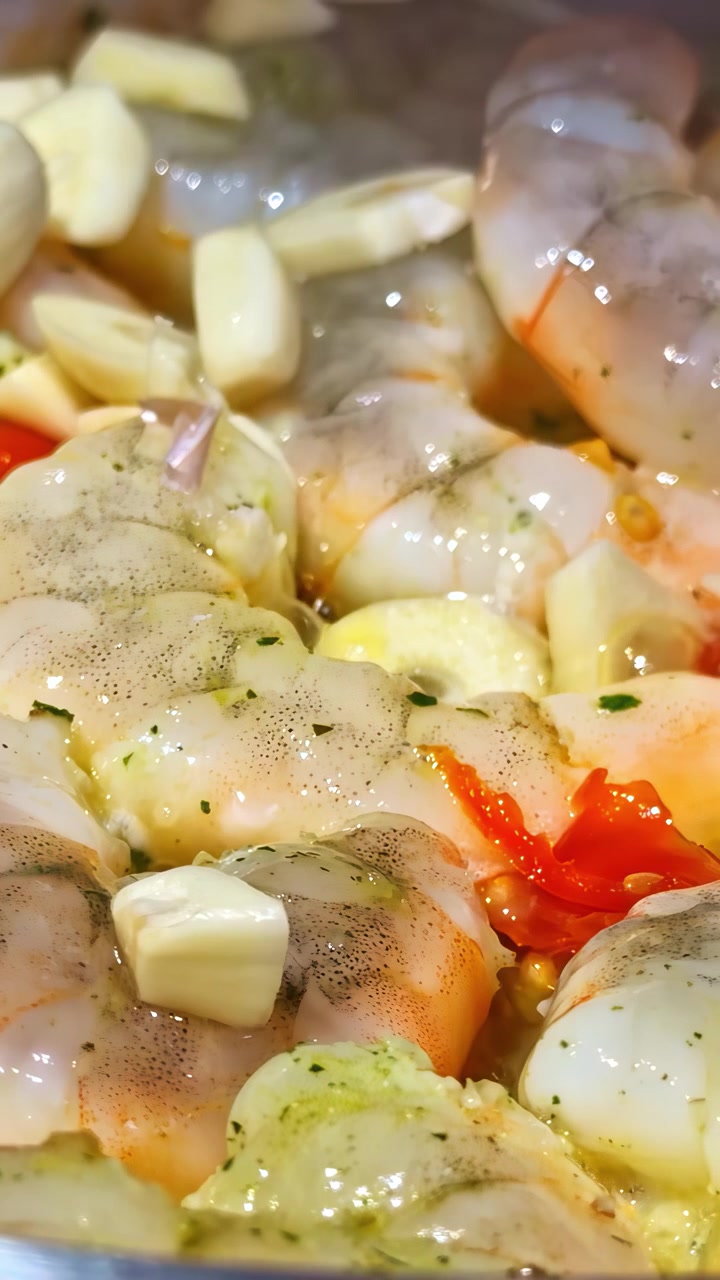 Raw shrimp marinating with garlic, butter, and chili in glossy seasoned seafood preparation, vertical bubbling cooking
