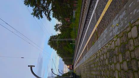 vertical video of an orange electrical train arriving to laagri station in estonia during summer time while sky is blue and slightly cloudy. poppy stones are on the ground at the platform, train stops