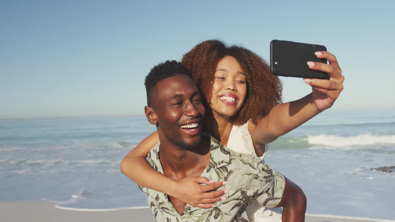 una pareja afroamericana tomando una selfie en la playa