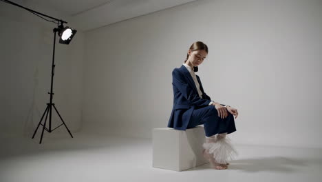 elegant woman in blue suit sitting on a white cube in a studio