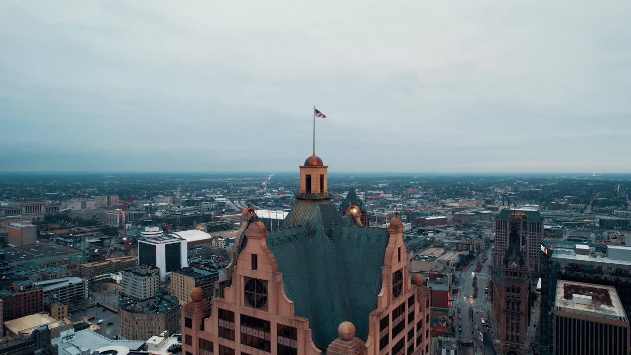 antena cinematográfica de la bandera estadounidense en la parte superior del edificio faison 100 este, milwaukee, wisconsin, estados unidos capturado al amanecer en un día nublado