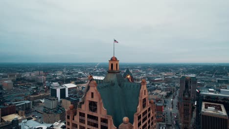 cinematic aerial of us flag on top of the faison building 100 east, milwaukee, wisconsin, usa captured at sunrise on a cloudy day