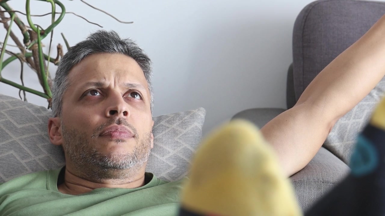 Uomo stressato che riposa sul divano mentre usa lo smartphone