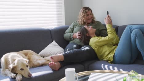pareja de lesbianas caucásicas sonriendo y sentadas en el sofá con el perro