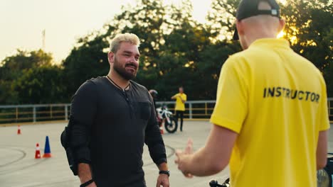 a male biker in protective gear with a thick beard communicates with a driving instructor in a yellow t-shirt