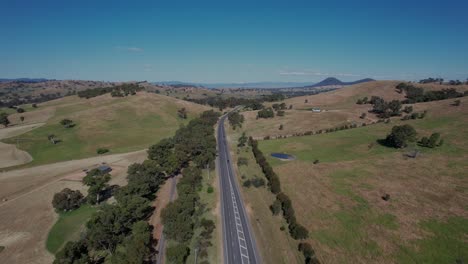 Aerial-lowering-straight-road-through-a-green-rural-landscape