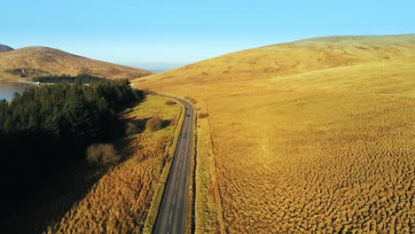 Car-moving-into-distance-traveling-through-silent-valley-Mourne-Mountains-Ireland-drone-shot