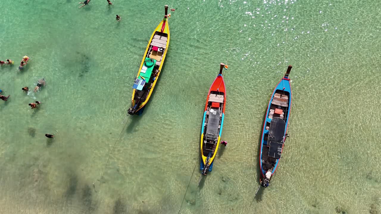 Drone footage captures vibrant boats and swimmers in clear waters off Phuket, Thailand, showcasing tropical leisure and vibrant colors