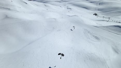 Dos-Paracaídas-De-Paracaidismo-Aterrizando-En-Pista-En-La-Estación-De-Esquí-De-Tignes,-Francia.