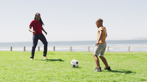 Video-Eines-Glücklichen-Afroamerikanischen-Vaters-Und-Sohnes,-Der-Draußen-Fußball-Spielt-Und-Spaß-Hat