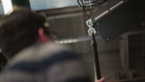 technician using boom pole to adjust lighting equipment in broadcast studio. professional media production environment with visible equipment and studio setup in background