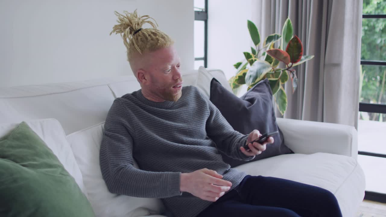 Man sitting on sofa, social media notifications growing around him, raising smartphone to film