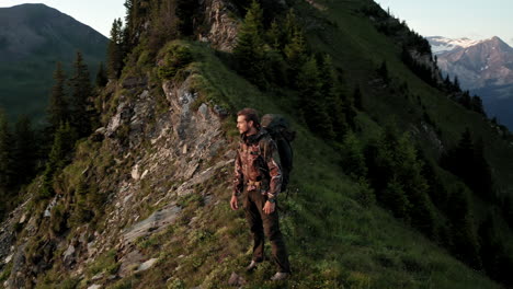 cinematic aerial shot of lone professional mountain hiker checking time on mountain peak at sunrise