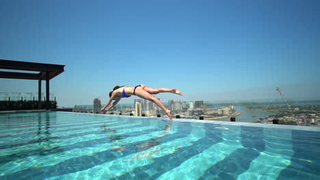 woman diving into a rooftop infinity pool in slow-motion overlooking the mekong river in downtown phnom pehn, cambodia