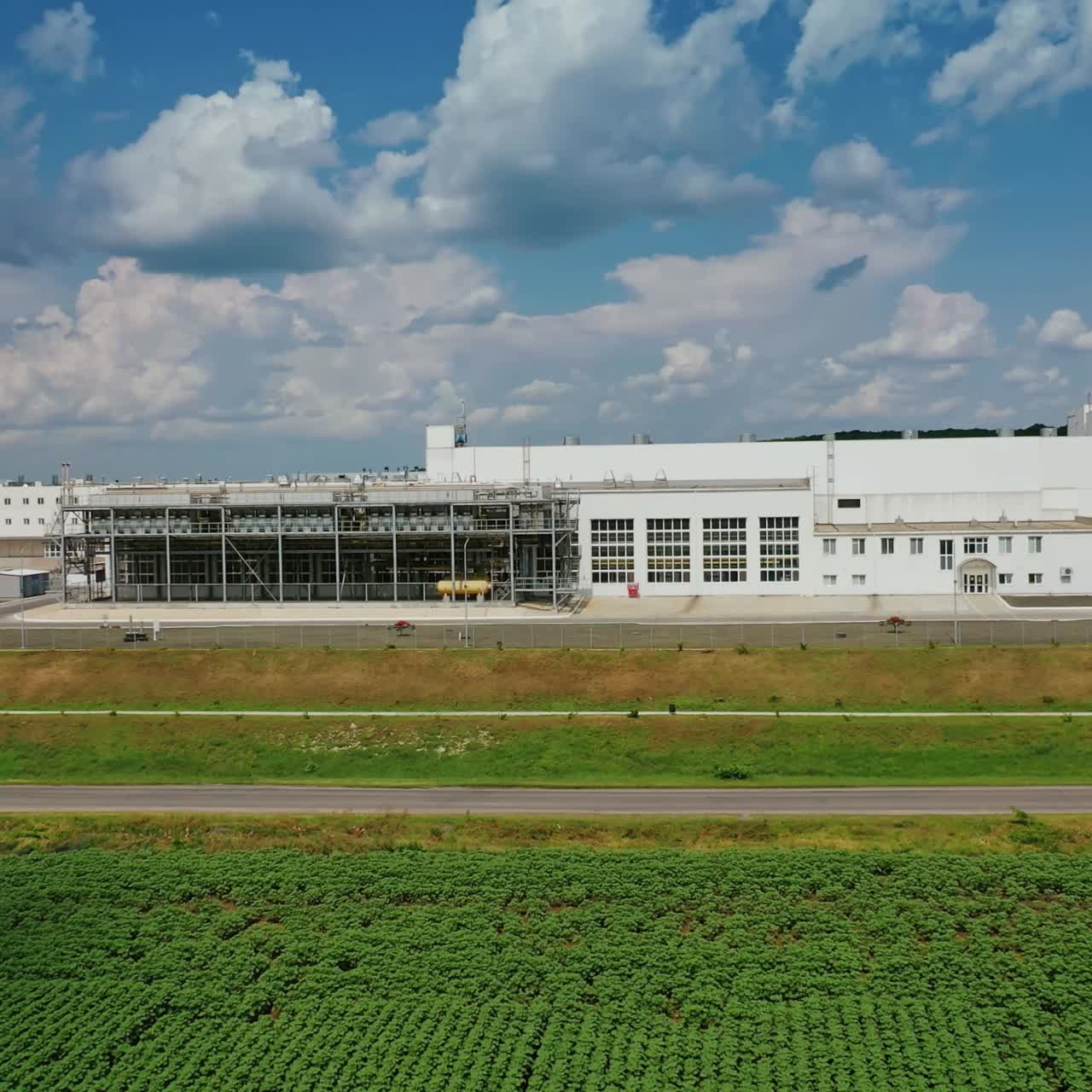 Industrial plant on green field. Huge territory with white buildings against blue sky. Exterior of factory in nature. Aerial view.