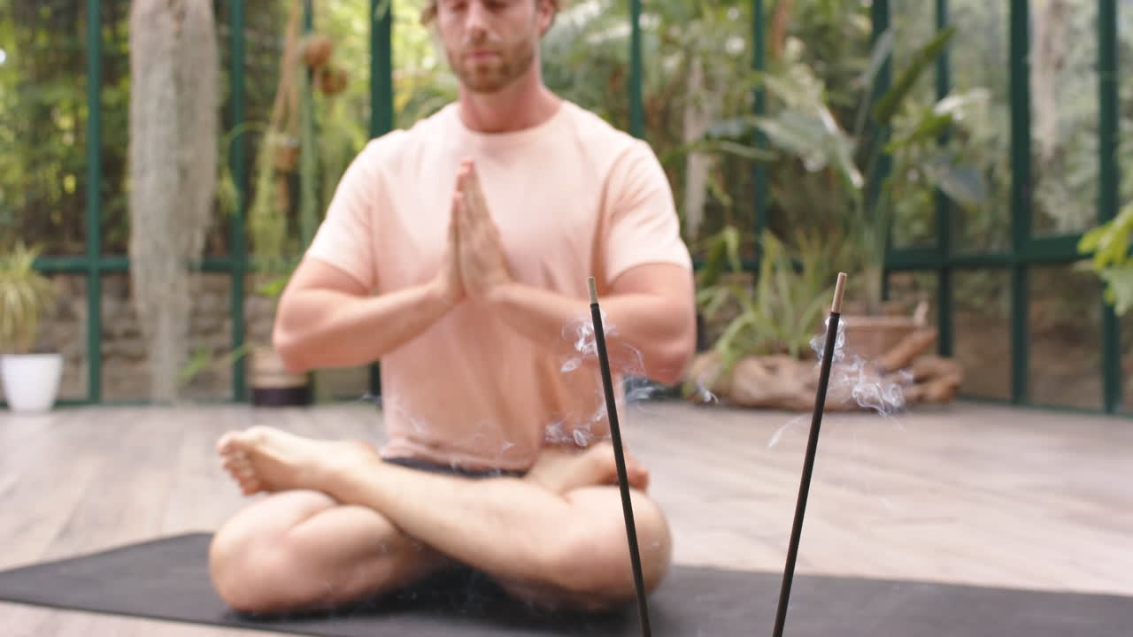 Yoga praktizieren: Mann sitzt im Schneidersitz, daneben brennen Räucherstäbchen.