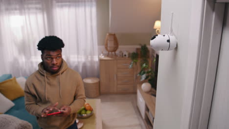 a man interacts with a home security camera in a living room using his smartphone
