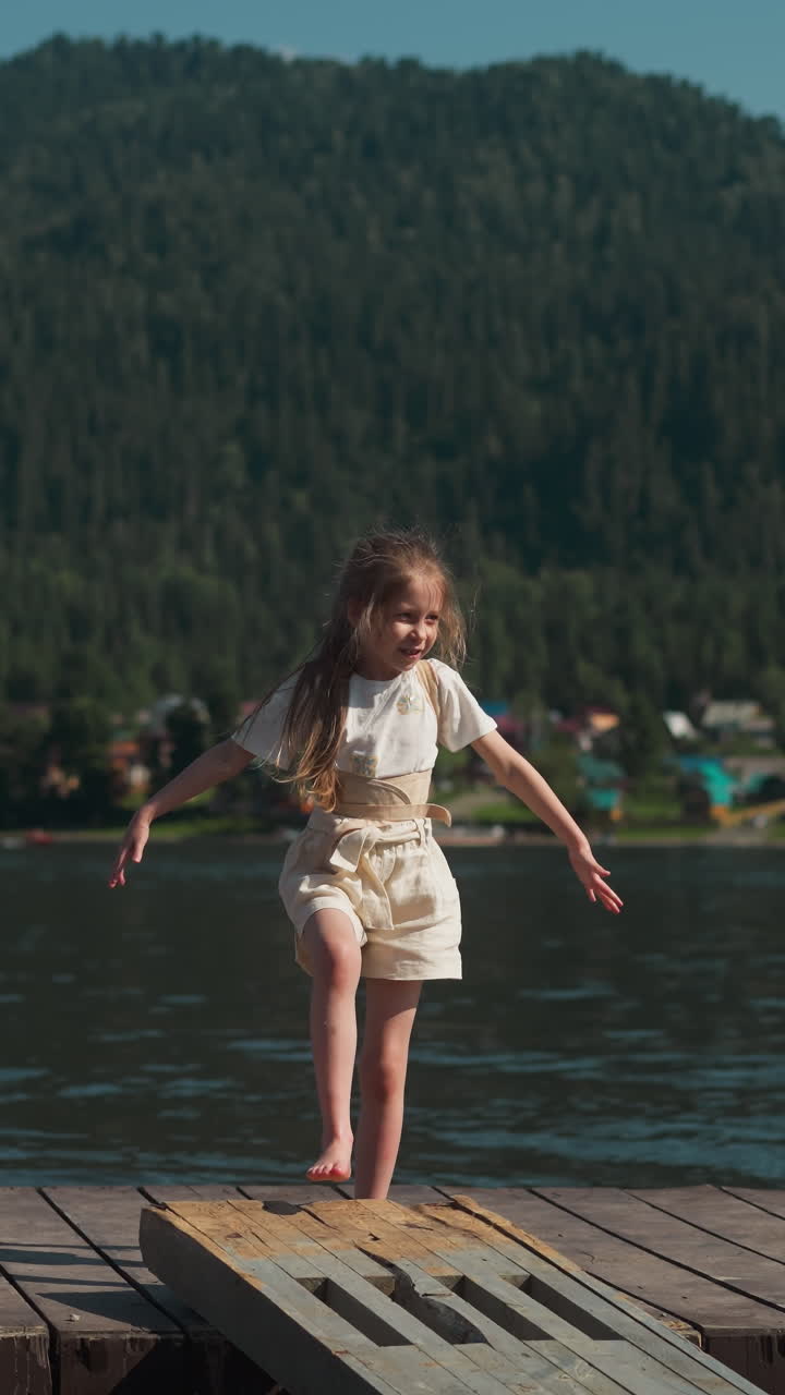 chica alegre agita los brazos a los lados moviéndose a lo largo del puente contra las pintorescas montañas. vacaciones en un lugar emocionante para los turistas. vacaciones para familias con niños