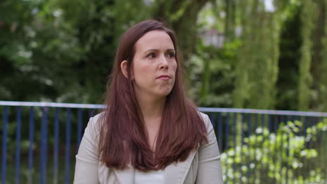 stressed and worried woman outdoors with financial worries about cost of living crisis debt and paying bills looking at mobile phone sitting on park bench