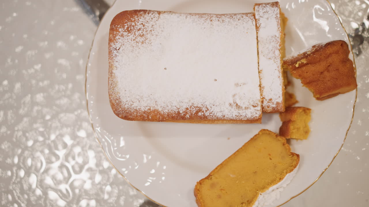 Overhead pumpkin loaf on white plate powdered sugar top food stylist slicing loaf with fork crumb fragments studio tabletop reflection bright even lighting sharp composition appetizing autumn spice