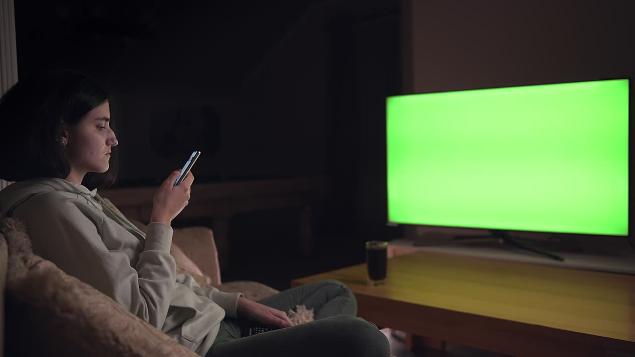 Ragazza bruna seduta sul divano, che guarda la TV e gioca ai giochi per cellulare, chroma key